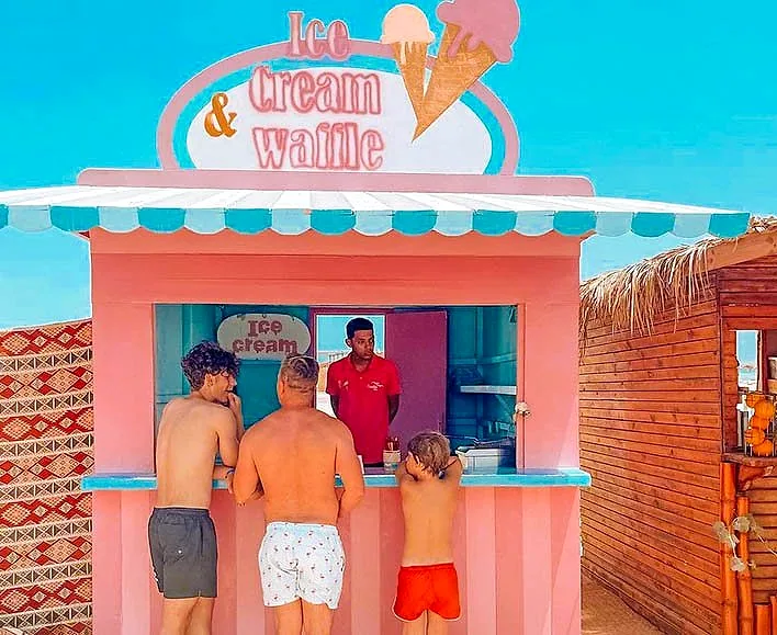 The ice cream and waffles kiosk at Paradise Island, painted pink and blue, with guests at the window.