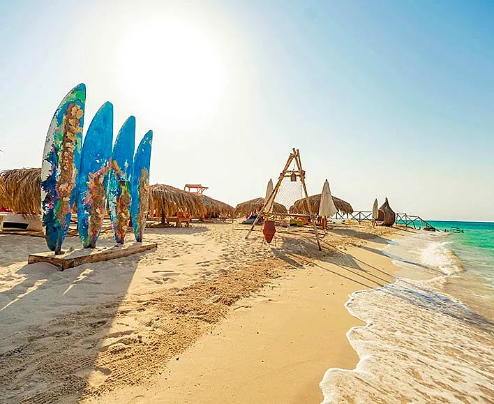 The shoreline at Paradise Island at low sun, with sun shades and loungers along the sand.