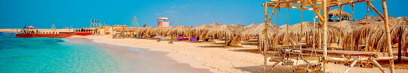 A wide view along the beach at Paradise Island, shades in a line and the jetty running out to the water.