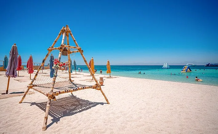Sun shades and a timber frame on the sand at Paradise Island, boats moored off the beach.