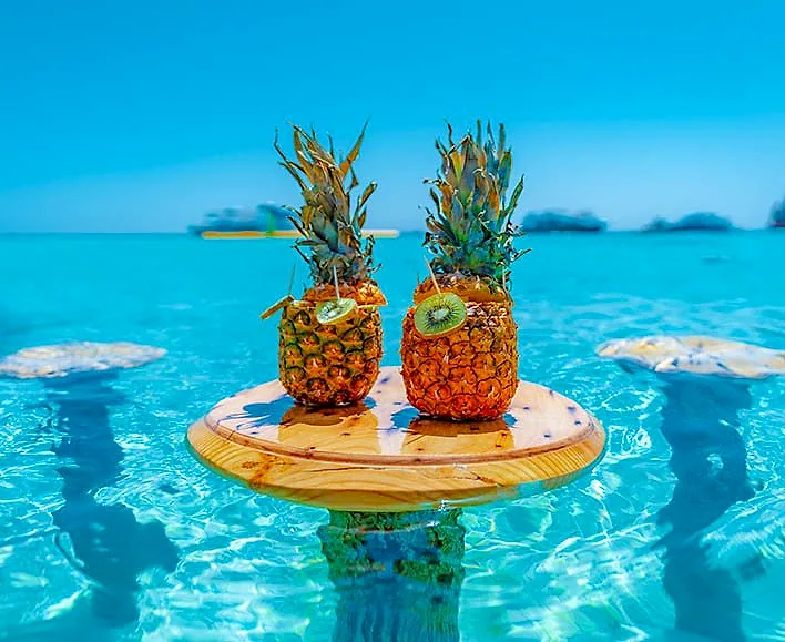 Two pineapples on a timber table standing in clear shallow water off the beach.